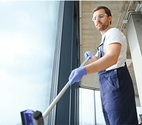 Gebäudereinigung - Mann mit Bart und Schutzbrille im blauem Overall putzt ein Fenster - Clean Team Solingen