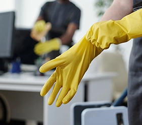 Unterhaltsreinigung - Reinigungskraft ziet gelbe Handschuhe an in einem Büro, um sich auf die Reinigung im Büro vorzubereiten - Clean Team Solingen